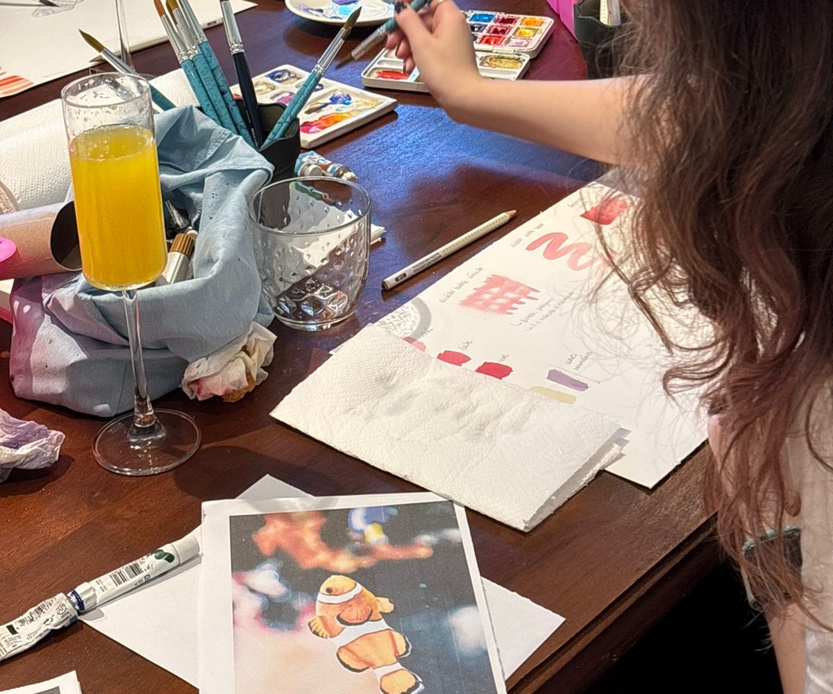 Materiais de aquarela, pincéis, paleta e pinturas sobre a mesa do workshop presencial da Duda Atelier, no Batel em Curitiba
